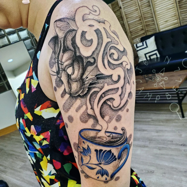 Alice in wonderland cheshire cat coming out of teacup smoke black and grey dotwork tattoo with pop of blue. Book a custom tattoo with John at Sacred Mandala Studio - Durham, NC.